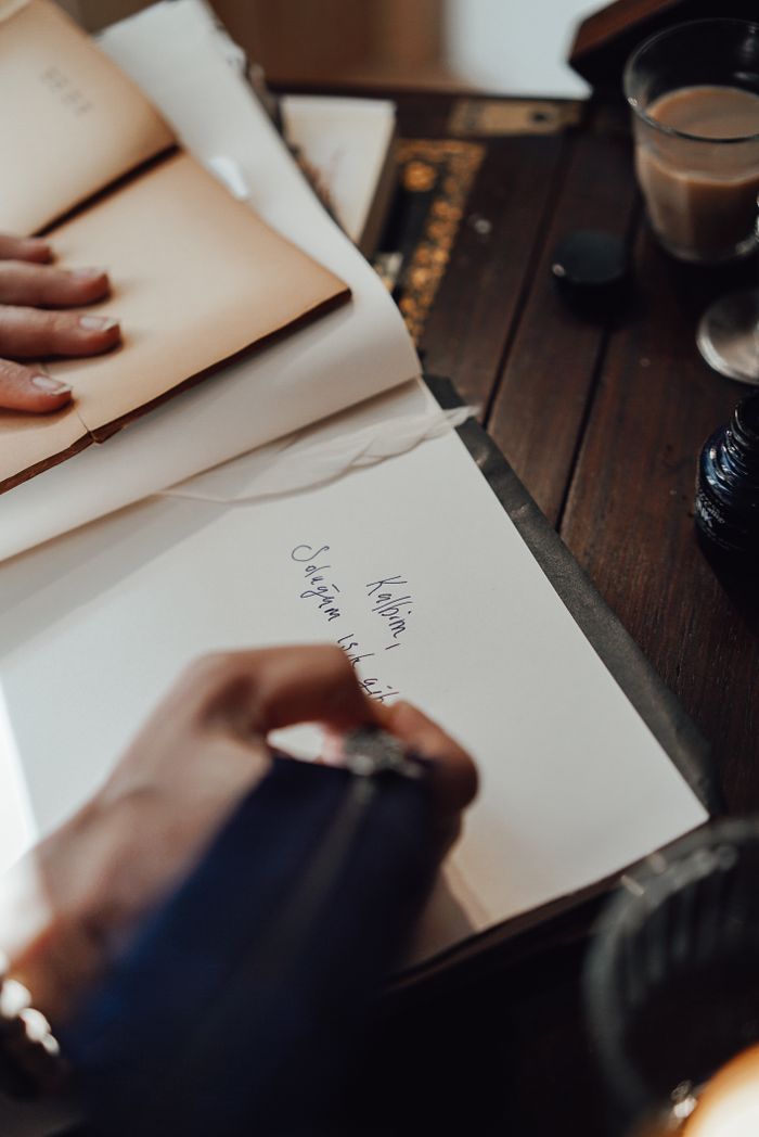 From above of crop unrecognizable female writer taking notes in notepad with feather at vintage table in house